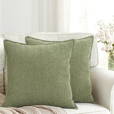 two green pillows sitting on top of a white couch next to a vase with flowers