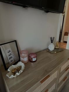 a tv mounted on the wall above a dresser with candles and other items sitting on it