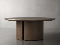 a round table with two wooden legs on a gray surface, in front of a white wall