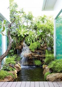 a small waterfall in the middle of a room with wooden flooring and plants around it