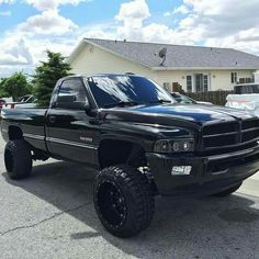 a black truck is parked in front of a house with large tires on the rims