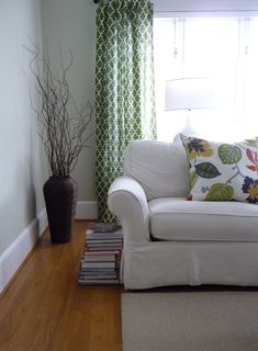 a living room with a white couch, green curtains and a lamp in the corner