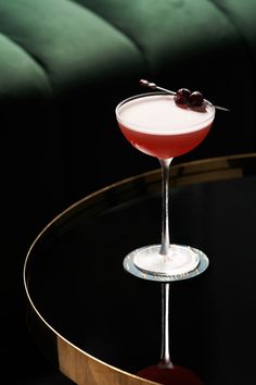 a cocktail sitting on top of a black table next to a green couch with an olive garnish