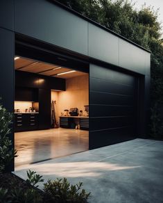 an open garage door in the middle of a concrete floored area with trees and bushes