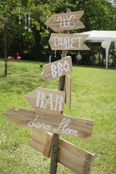 several wooden signs pointing in different directions on a pole with grass and trees in the background