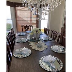 a dining room table set with place settings and crystal chandelier hanging from the ceiling