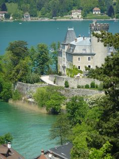 an old castle sitting on top of a hill next to the water with trees around it