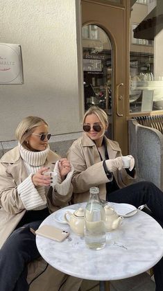 two women sitting on a bench in front of a store window, one holding the other's hand