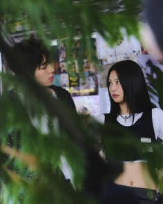 two young people standing next to each other in front of a green leafy tree