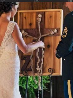 a bride and groom standing in front of a wooden cross with ropes hanging from it