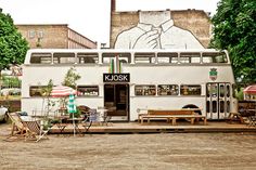 a double decker bus parked in front of a building with tables and chairs around it