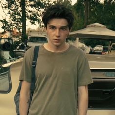 a young man standing in front of a car with his hand on his hip and looking at the camera