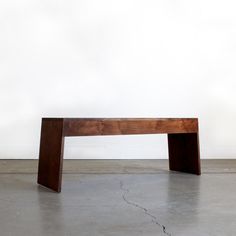 a wooden bench sitting on top of a cement floor in front of a white wall