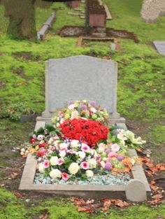 a headstone with flowers on it in the middle of a grassy area next to a tree