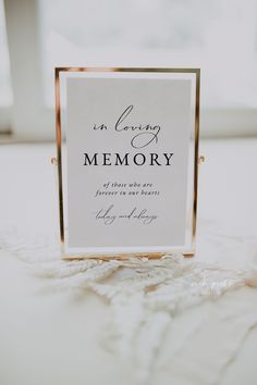 a sign that says in loving memory on the floor next to a window with white curtains