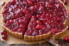 a tart with cranberry sauce is cut into pieces and sits on a piece of parchment paper