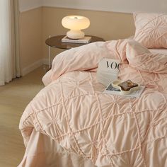 a bed with pink comforter and pillows on top of it next to a lamp