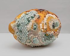 an orange covered in lots of beads sitting on top of a white table next to a gray wall