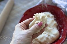 a person holding food in their hand and kneading it into a red bowl