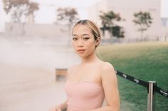 a young woman in a pink dress standing next to a metal fence and grass area