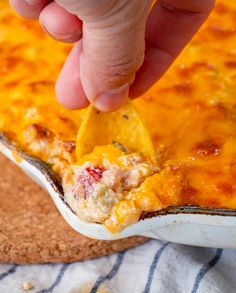 a hand dipping a tortilla chip into a casserole dish with cheese