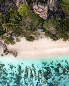 an aerial view of two people walking on the beach in front of some rocks and trees