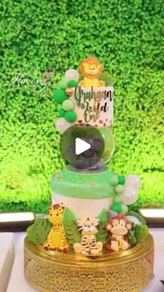 a three tiered cake with animals and balloons on it's top, sitting in front of a green wall