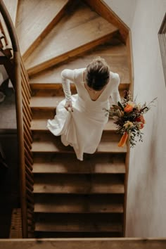 a woman in a white dress is walking down the stairs with flowers on her hand