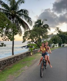 two people riding on the back of a bike down a road next to the ocean