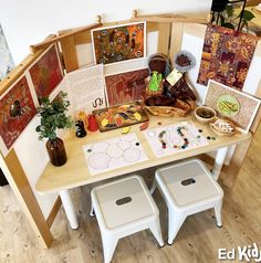 a wooden table topped with lots of cards and pictures next to two white stools