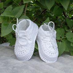 white crocheted baby shoes sitting on top of a cement ground next to green leaves