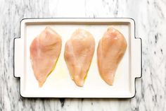 three pieces of raw chicken on a white tray with marble counter top in the background