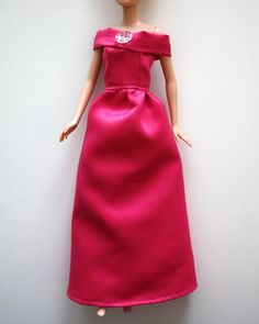 a barbie doll wearing a pink dress and tiara, standing against a white wall