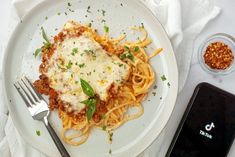 a white plate topped with pasta and sauce next to a cell phone on top of a table