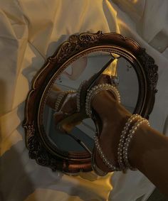 a woman's hand holding a mirror with pearls on it