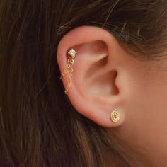 a woman's ear is adorned with gold chains and a single white diamond in the middle