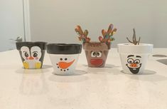 four coffee cups decorated to look like reindeers and snowmen with faces painted on them