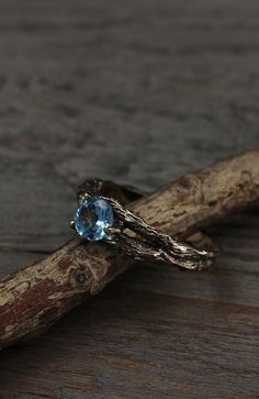 a ring with a blue topaz sits on a piece of driftwood next to a branch