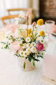 a vase filled with lots of flowers on top of a white tablecloth covered table