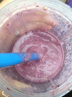 a blender filled with pink liquid sitting on top of a wooden table next to a blue plastic spoon