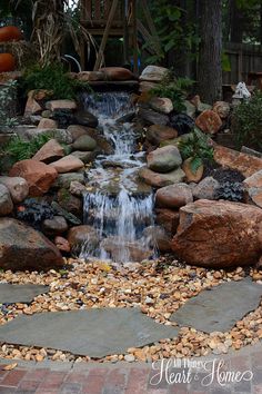 a small waterfall in the middle of a garden with rocks and gravel around it's edges