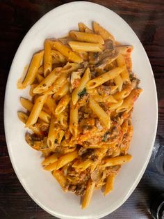 a white plate topped with pasta and meat covered in sauce on top of a wooden table