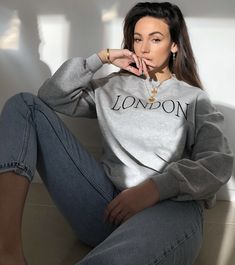 a woman sitting on the floor with her hands in her mouth and wearing a grey sweatshirt