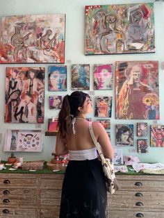 a woman standing in front of a wall covered with pictures and paintings, looking up at the sky