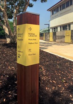 a wooden post with a yellow sign on it in front of a tree and building