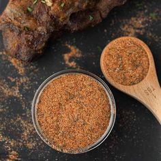 a wooden spoon next to a glass bowl filled with seasoning on top of a black surface