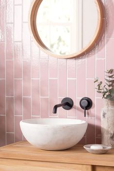 a white bowl sink sitting on top of a wooden counter next to a round mirror