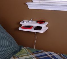 a bed with a pillow and a wall shelf on the side that has an electronic device plugged into it