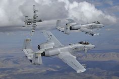 four fighter jets flying in the sky with mountains in the back ground and clouds in the background