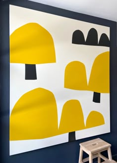 a yellow and black painting hangs on the wall next to a wooden stool in front of it